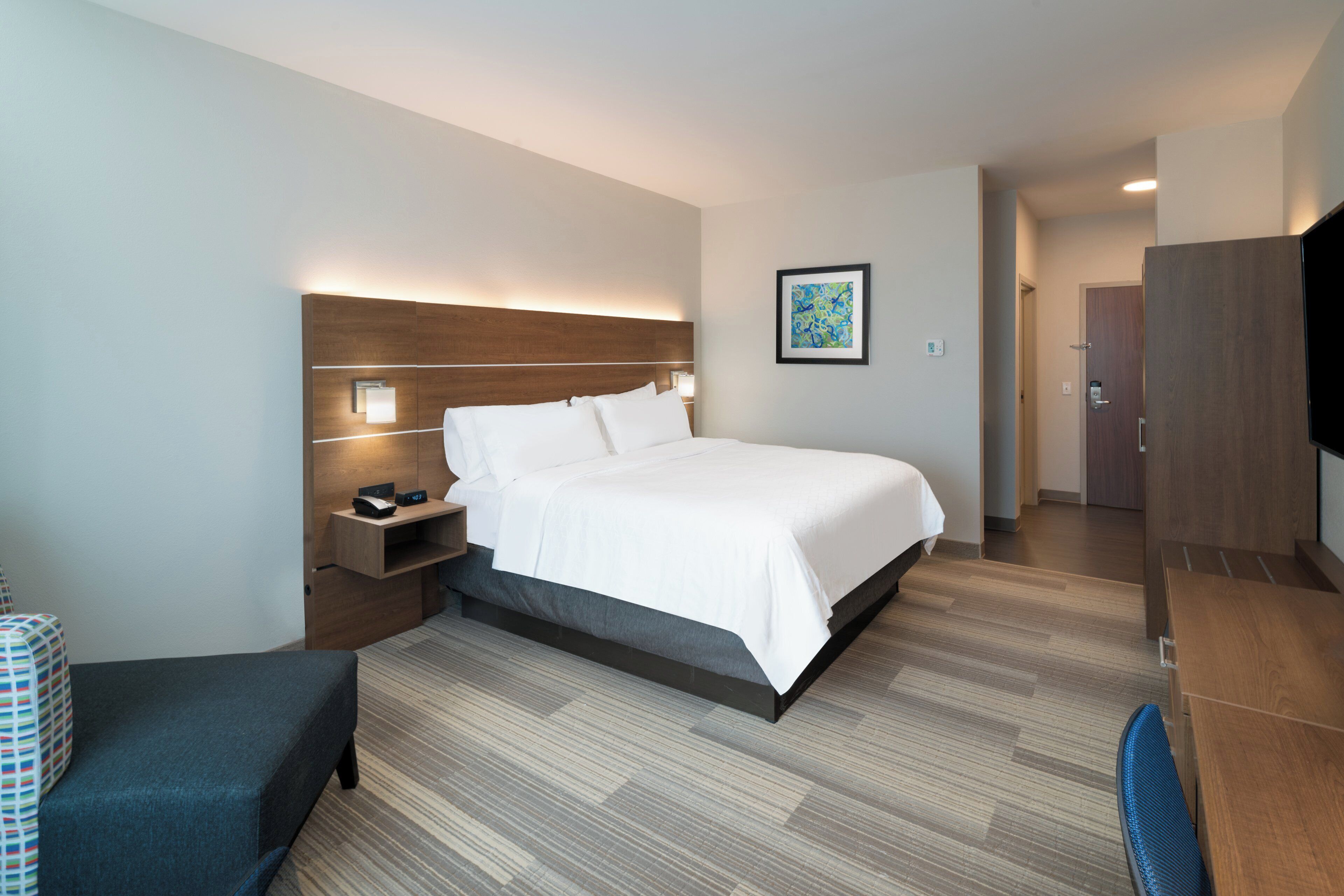 A hotel room with a bed, bedside table, lamp, and a TV.