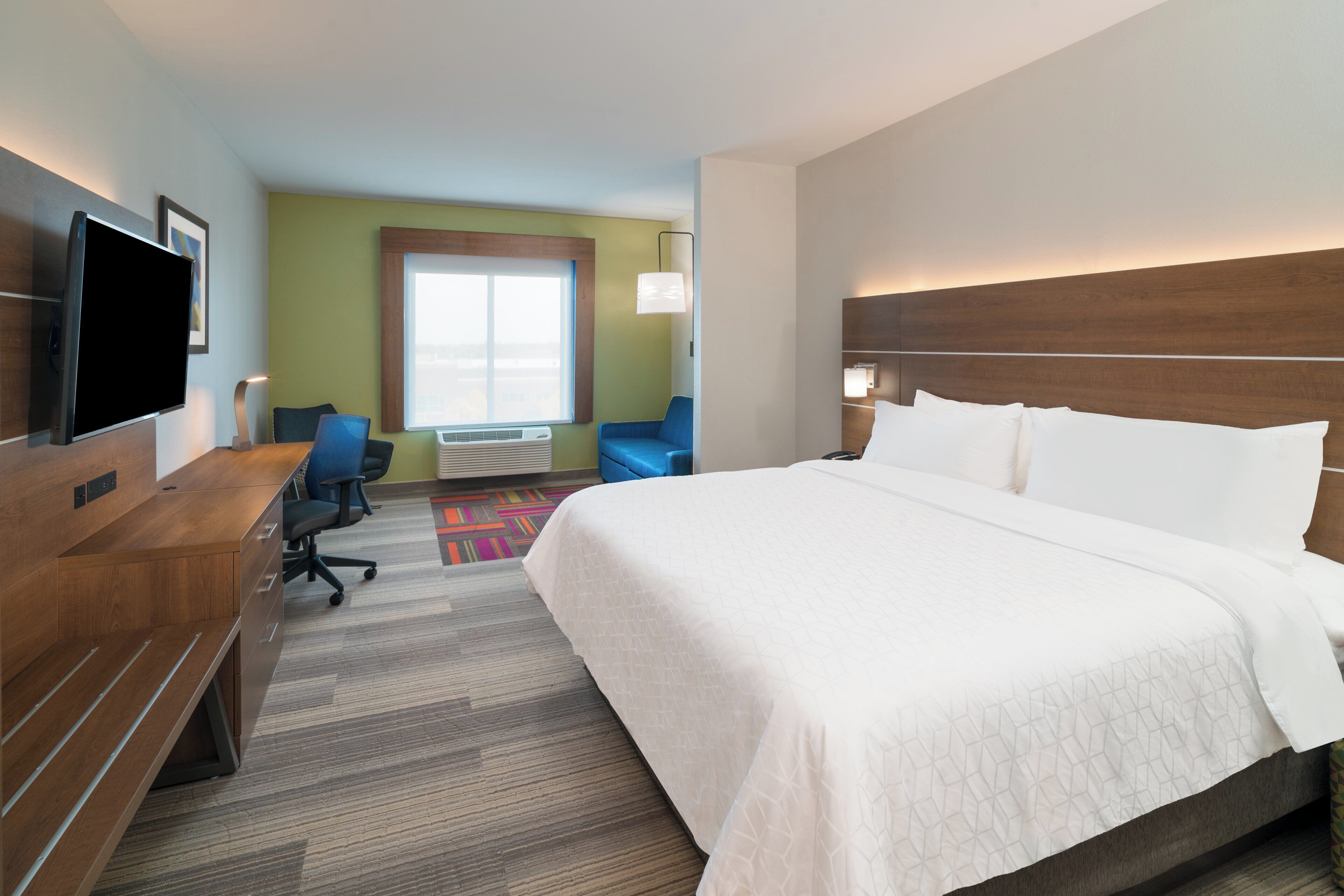 A hotel room with a large bed, a desk, a chair, a television, and a window with a view.