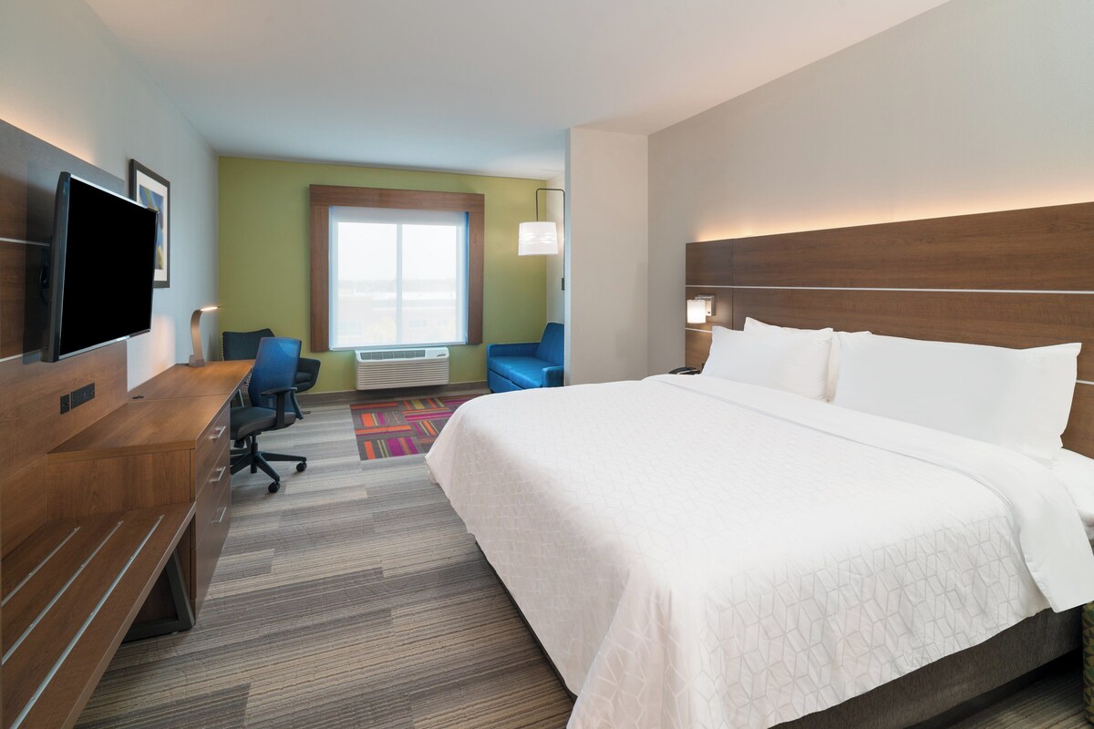 A hotel room with a large bed, a desk, a chair, a television, and a window with a view.