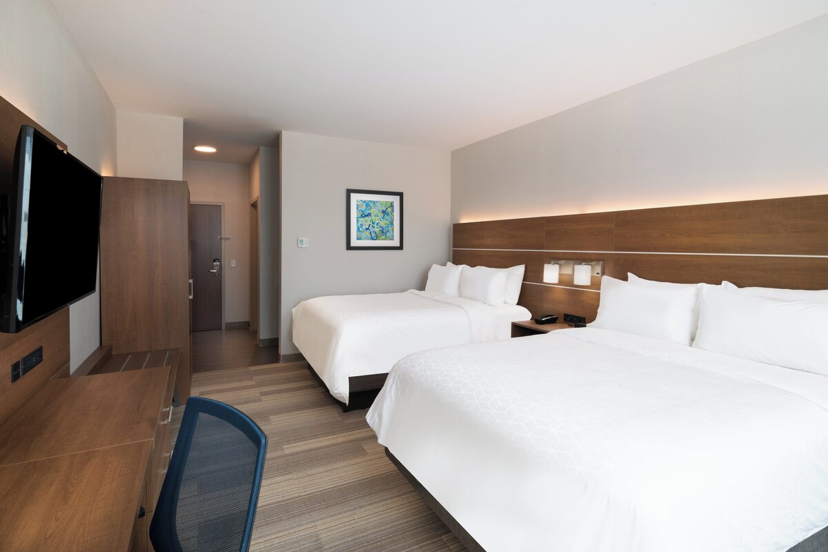A hotel room with two beds, a desk, a TV, and a painting on the wall.