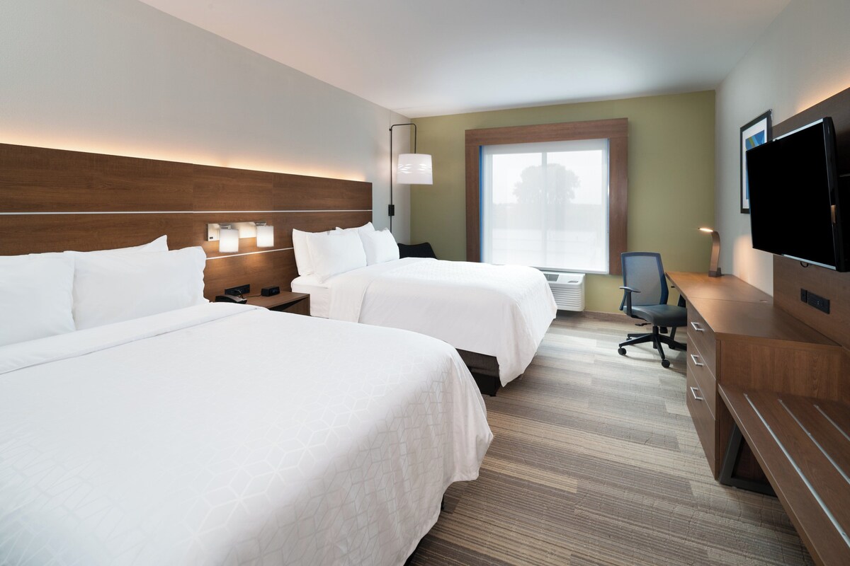 A hotel room with two beds, a desk with a chair, a television, and a window with blinds.