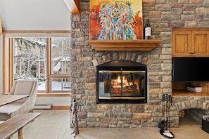 A stone fireplace with a fire, a painting above it, and a TV on the right.