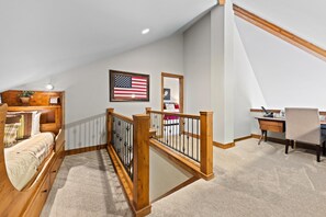 Une chambre avec un lit en bois, un bureau et un ordinateur. On y trouve un escalier avec une rampe en bois.