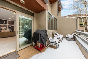 Un espace extérieur abrité avec un barbecue, une porte-fenêtre coulissante et une terrasse recouverte de neige.