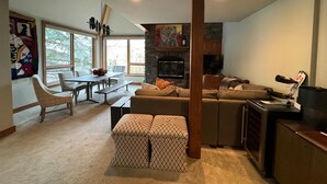 Una sala de estar moderna con chimenea, un comedor con mesa y sillas, y una zona de estar acogedora con sofá y reposapiés.