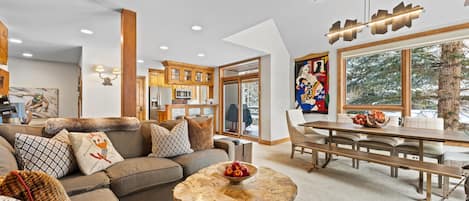 A modern living room with a sectional sofa, a marble coffee table, and a dining area with a wooden table and chairs.