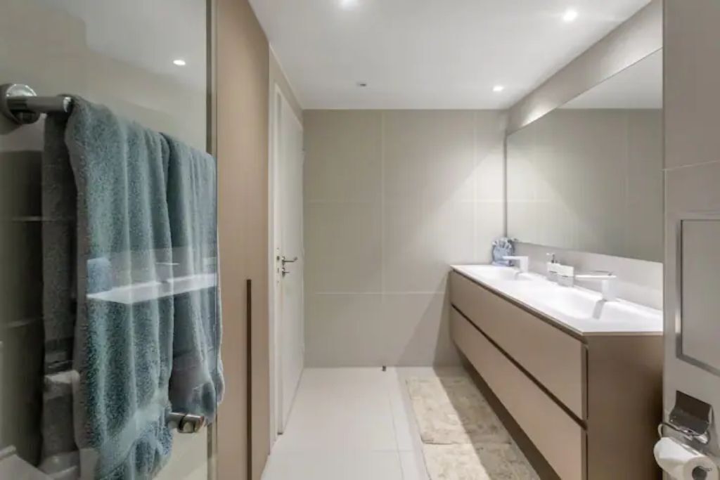 Een moderne badkamer met een douchecabine van glas, een grote spiegel en een wastafelmeubel met twee wastafels.