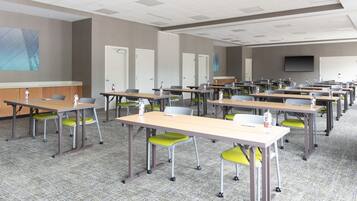 A conference room with multiple tables and chairs, a projector screen, and a whiteboard.
