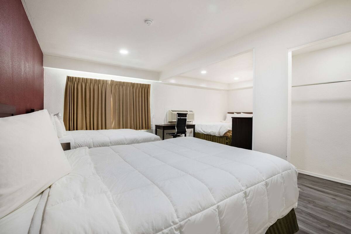 A hotel room with two beds, a desk, a chair, and a wardrobe.