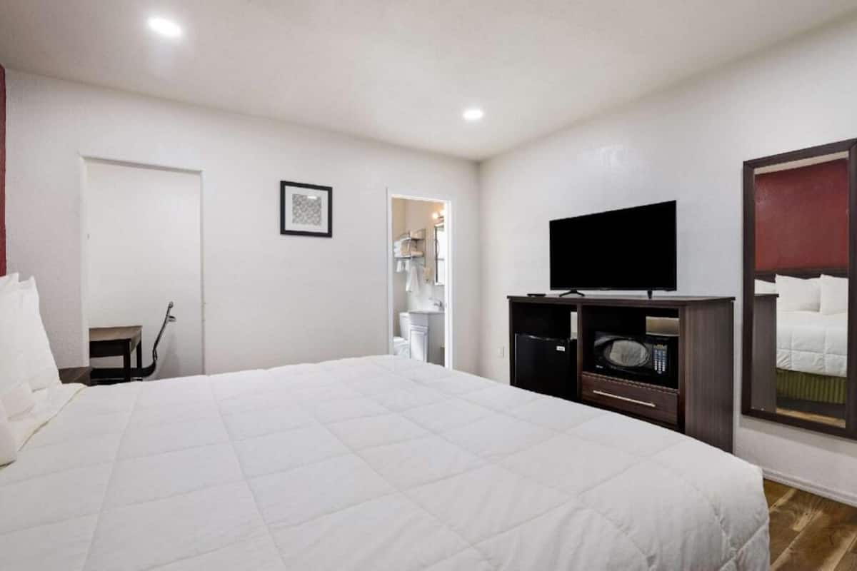 A hotel room with a large bed, a television, a microwave, and a door leading to a bathroom.