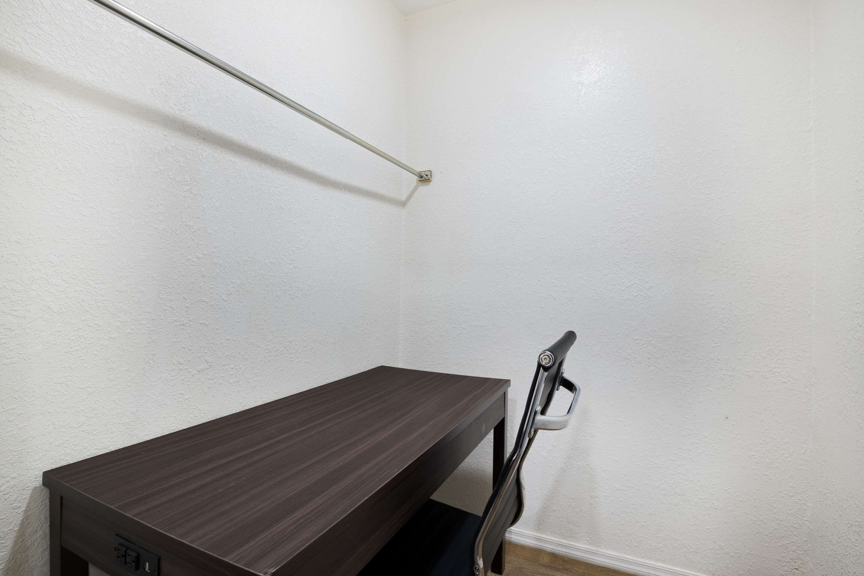 Un escritorio de madera oscura y pequeño con un estante metálico encima, pegado a una pared blanca.