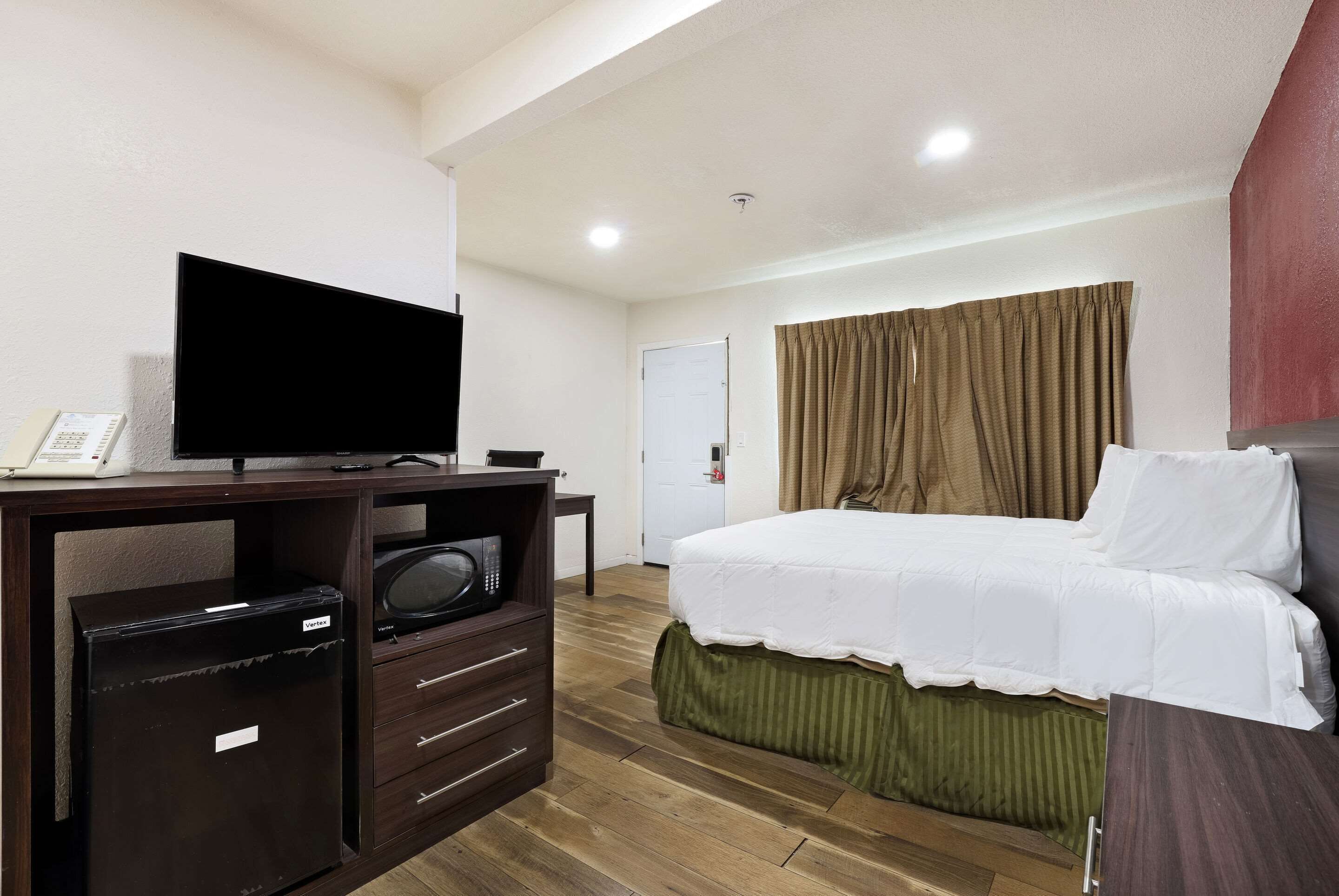 A hotel room with a bed, a TV, a desk with drawers, a small safe, and a door.