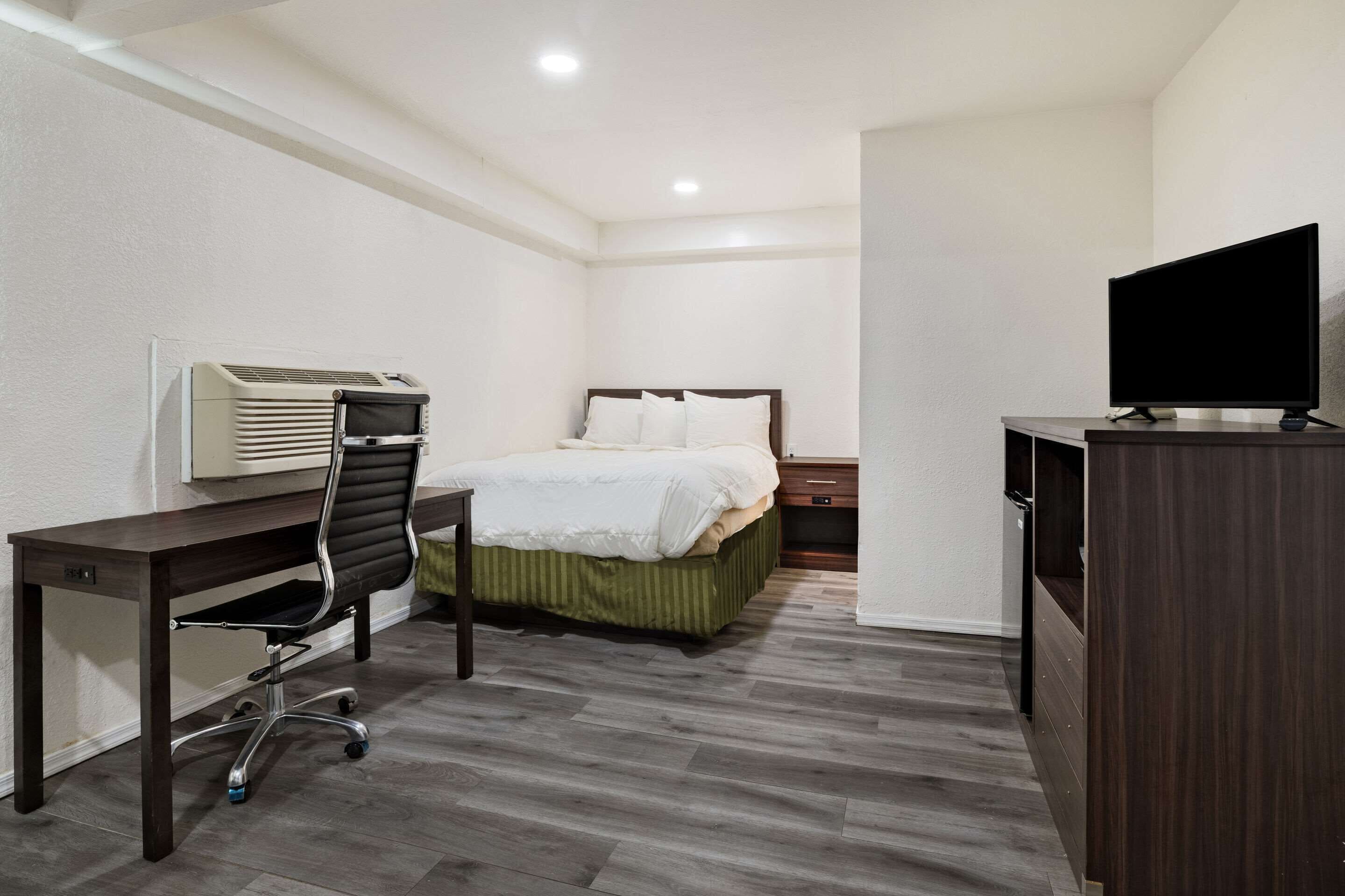 Ein Hotelzimmer mit Bett, Schreibtisch, Stuhl, Fernseher und Klimaanlage.