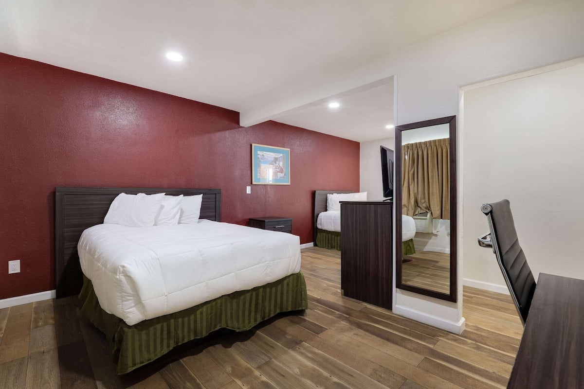 A hotel room with a large bed, a bedside table, a mirror, and a wooden floor.