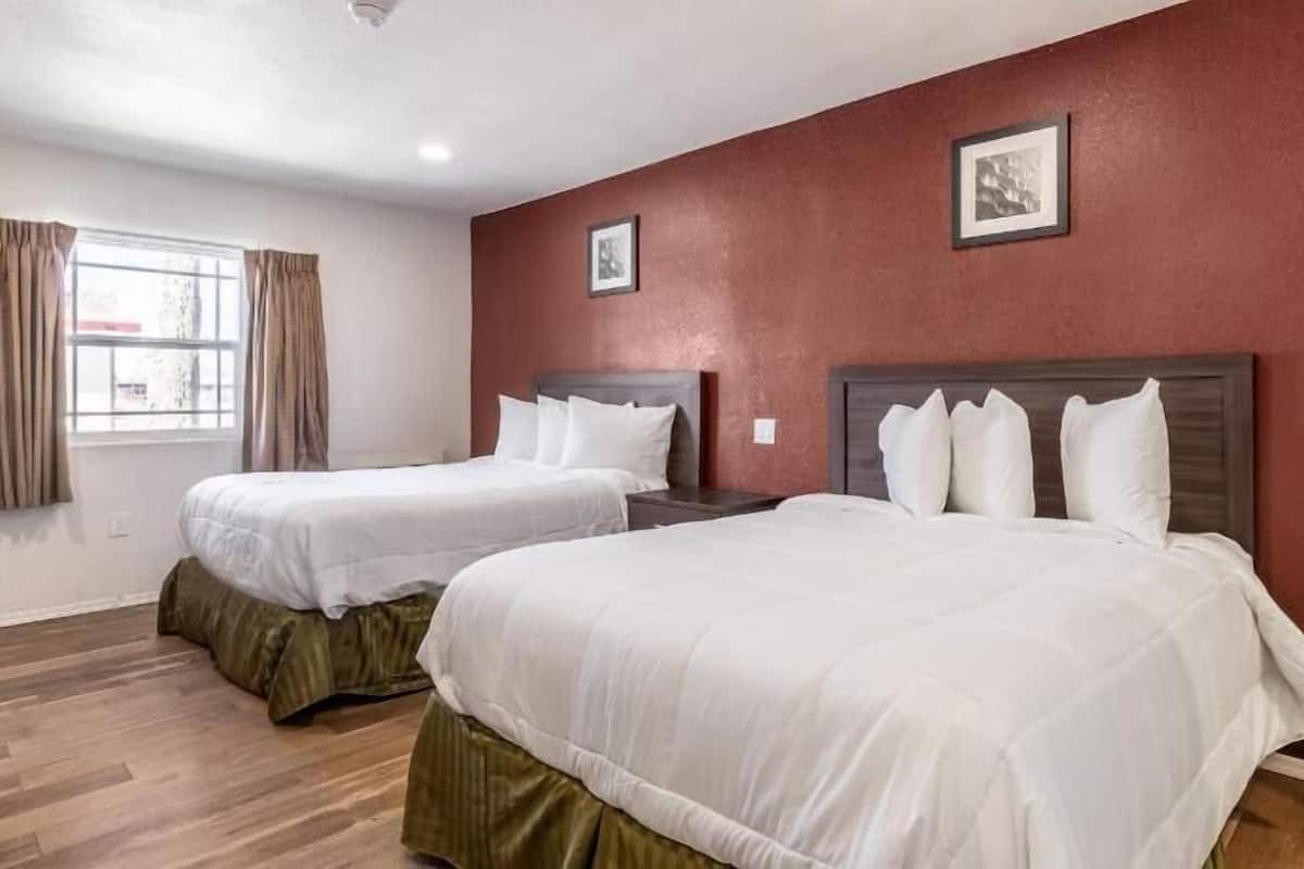 A hotel room with two beds, wooden flooring, a window with curtains, and two framed pictures on the wall.