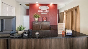 A hotel reception desk with a red wall, a plant, a 'Thank You For Staying With Us' sign, and a 'The faster way to rewards' sign.