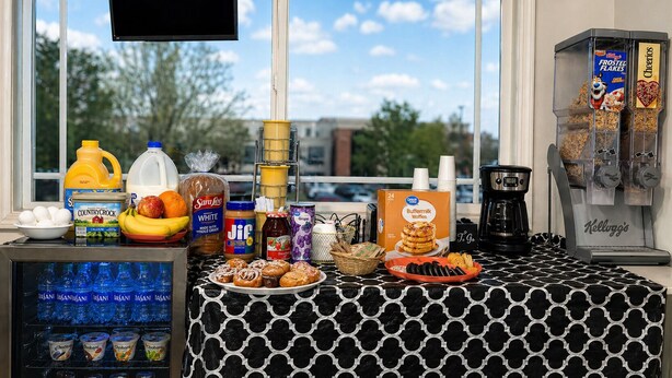 A breakfast bar with various food items, a coffee machine, and a refrigerator stocked with beverages.