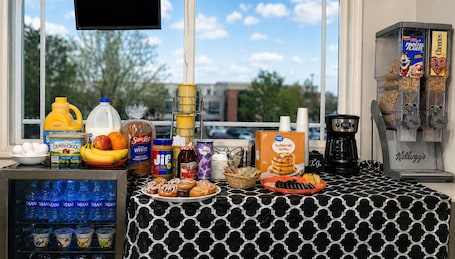 A breakfast bar with various food items, a coffee machine, and a refrigerator stocked with beverages.