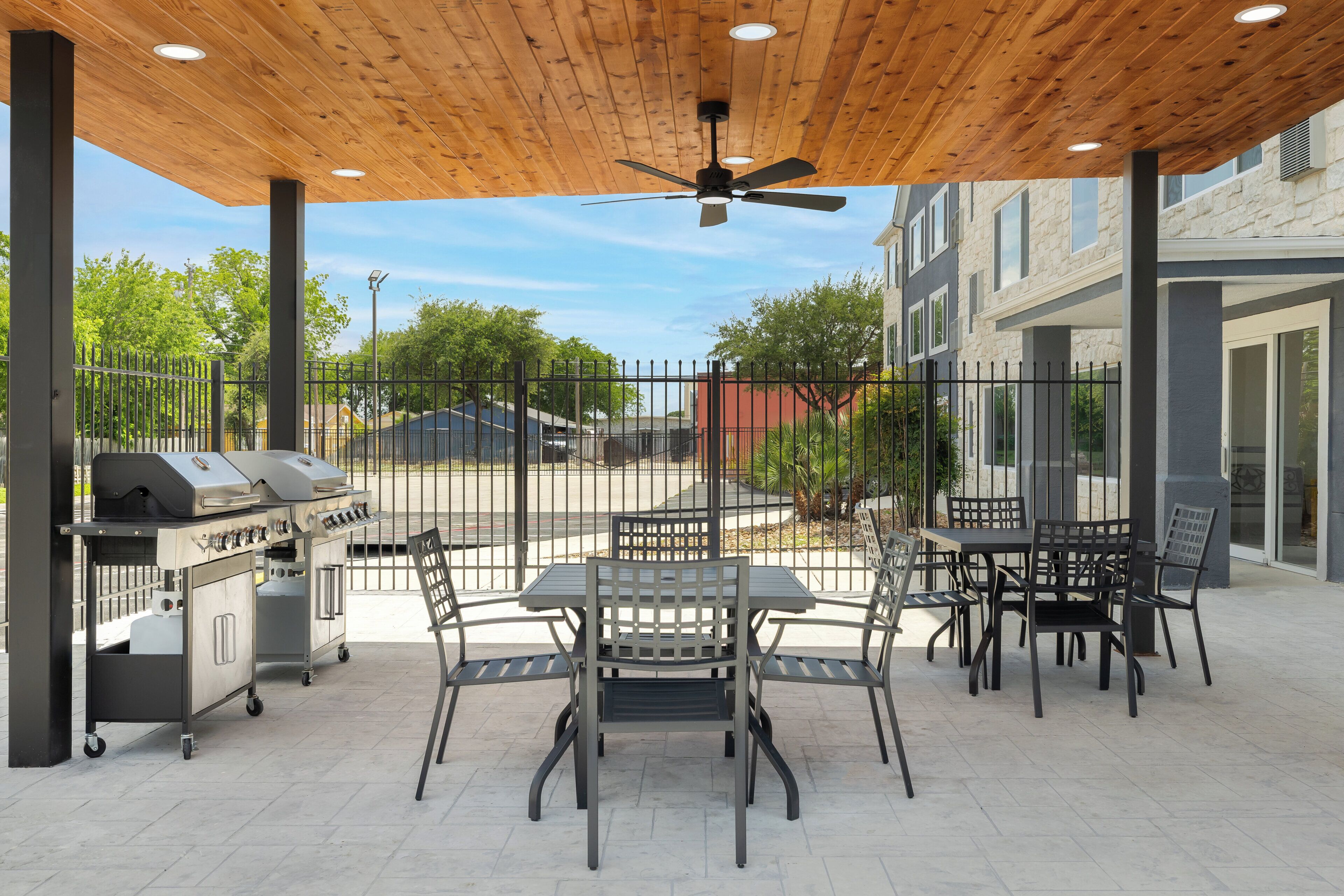 An outdoor patio with a grill, table, and chairs, surrounded by a fence and buildings.