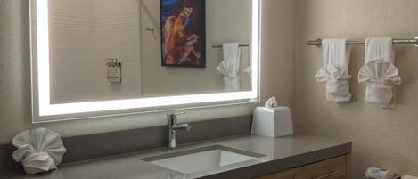 A bathroom with a large mirror, two sinks, a towel rack, and a trash bin.
