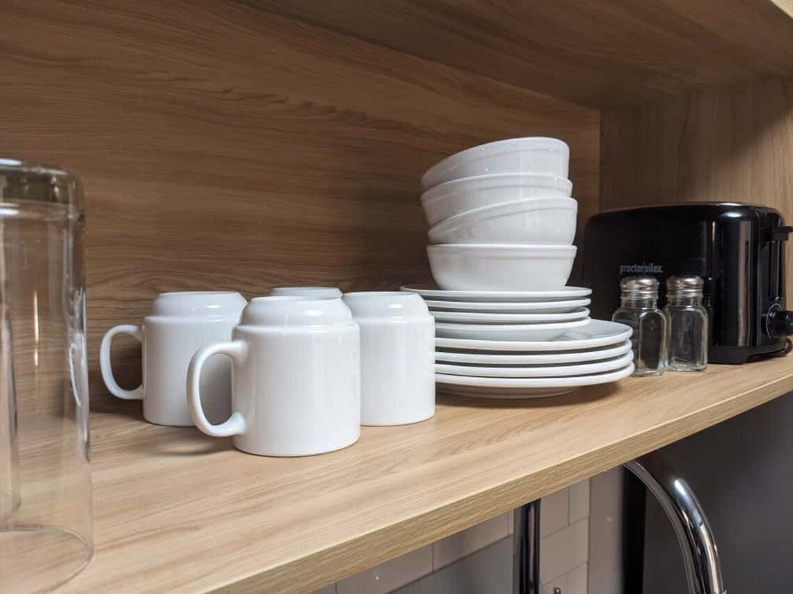 A kitchen counter with white mugs, stacked plates, a coffee maker, and salt and pepper shakers.
