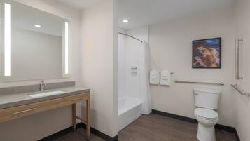 A bathroom with a sink, mirror, shower, toilet, and a framed picture on the wall.