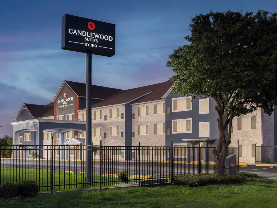 Ett hotell med en skylt som visar texten ”Candlewood Suites by IHG”, med en modern byggnad som har många fönster och en välskött gräsmatta.