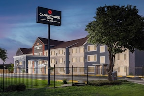 A hotel with a sign reading 'Candlewood Suites by IHG,' featuring a modern building with multiple windows and a well-maintained lawn. - Candlewood Suites San Antonio - Fort Sam Houston (San Antonio)