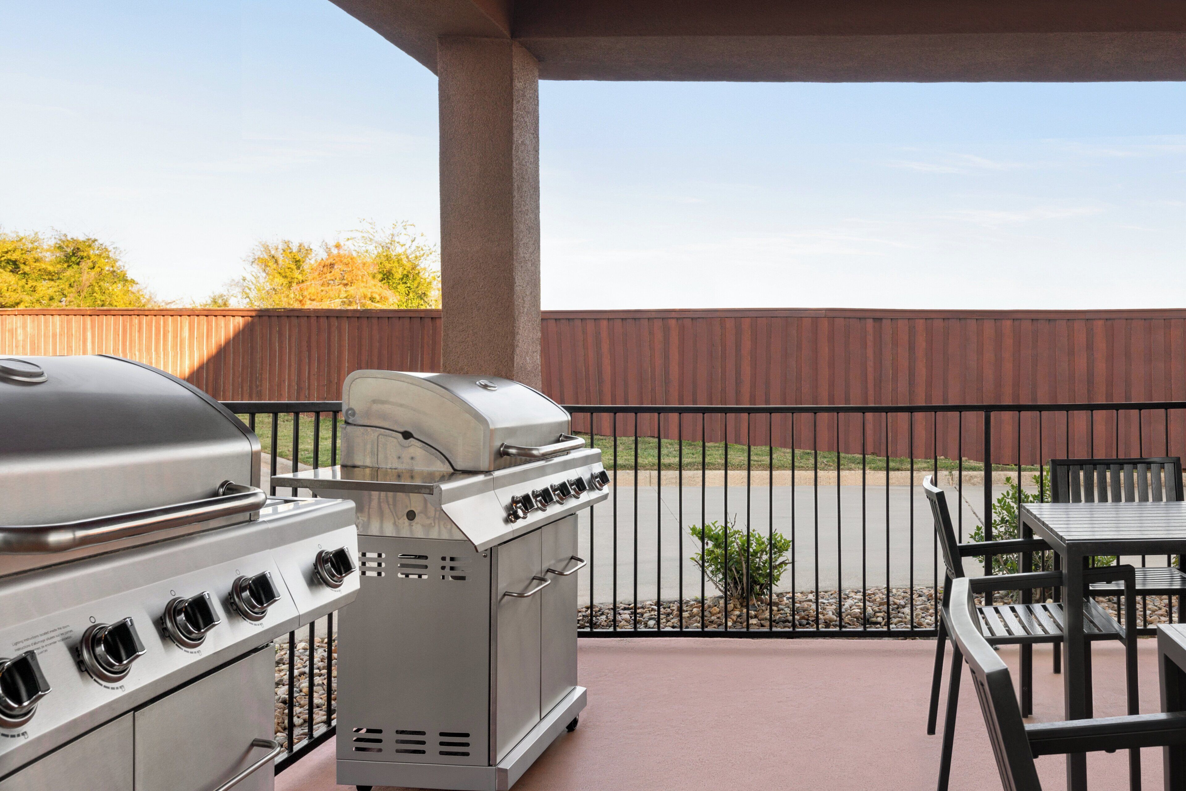 A patio with a grill, outdoor table, and chairs.