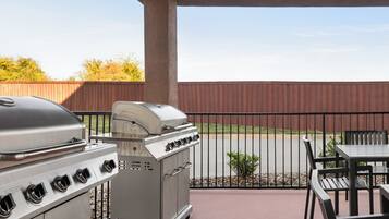 A patio with a grill, outdoor table, and chairs.