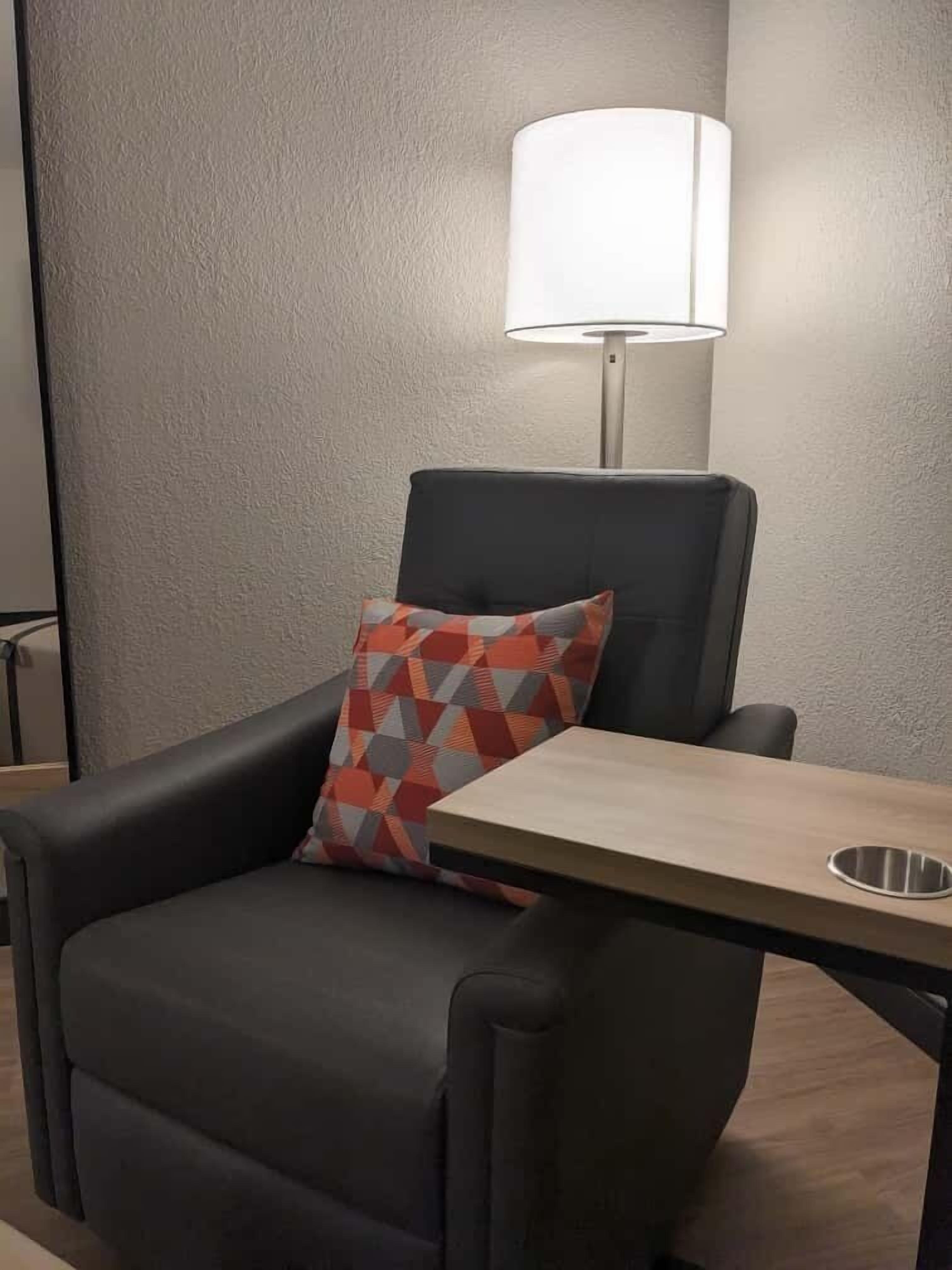 A modern armchair with a geometric-patterned pillow, a small table with a metal tray, and a floor lamp.
