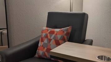 A modern armchair with a geometric-patterned pillow, a small table with a metal tray, and a floor lamp.