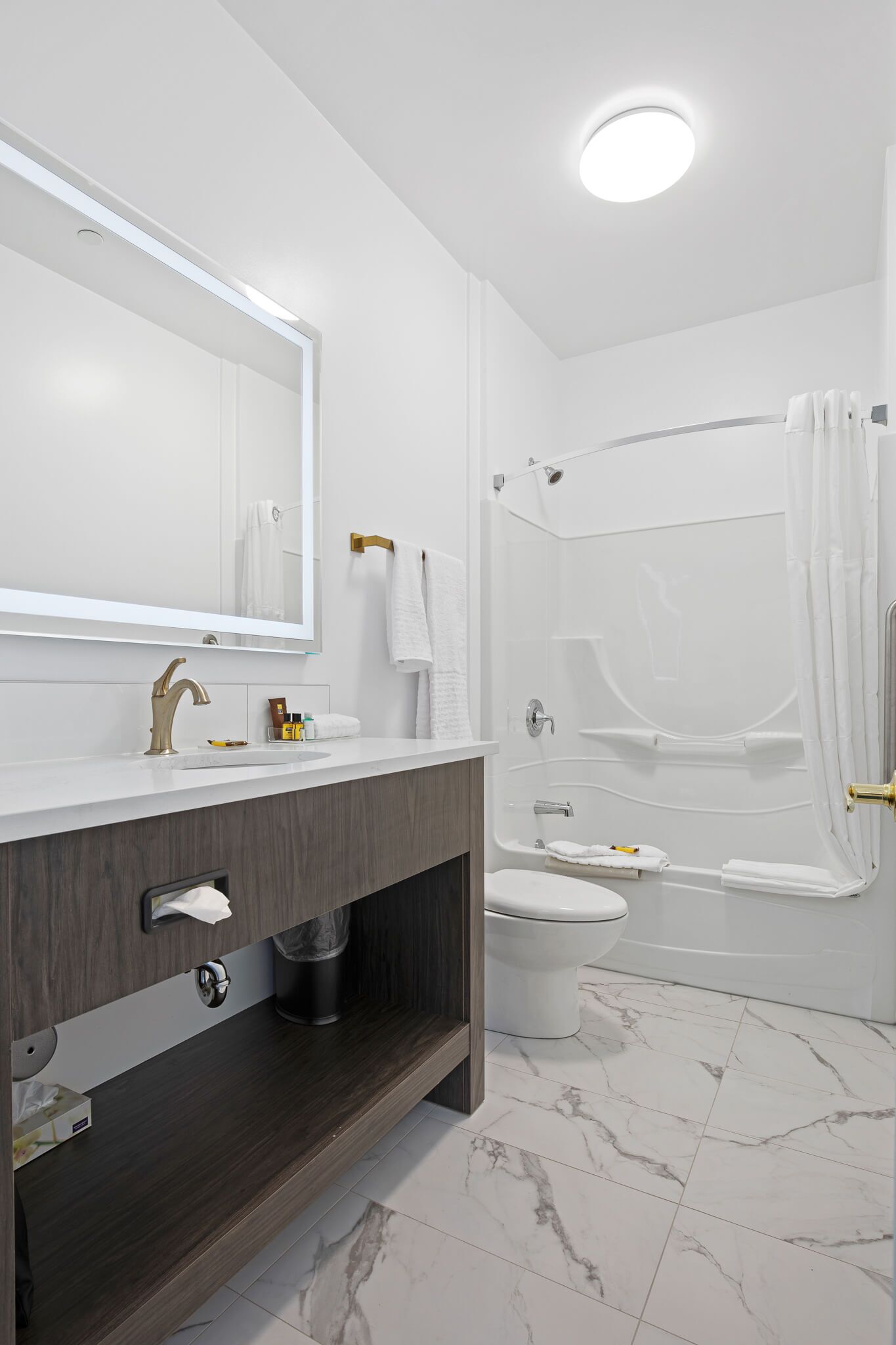A modern bathroom with a white vanity, a large mirror, a toilet, and a bathtub with a shower curtain.