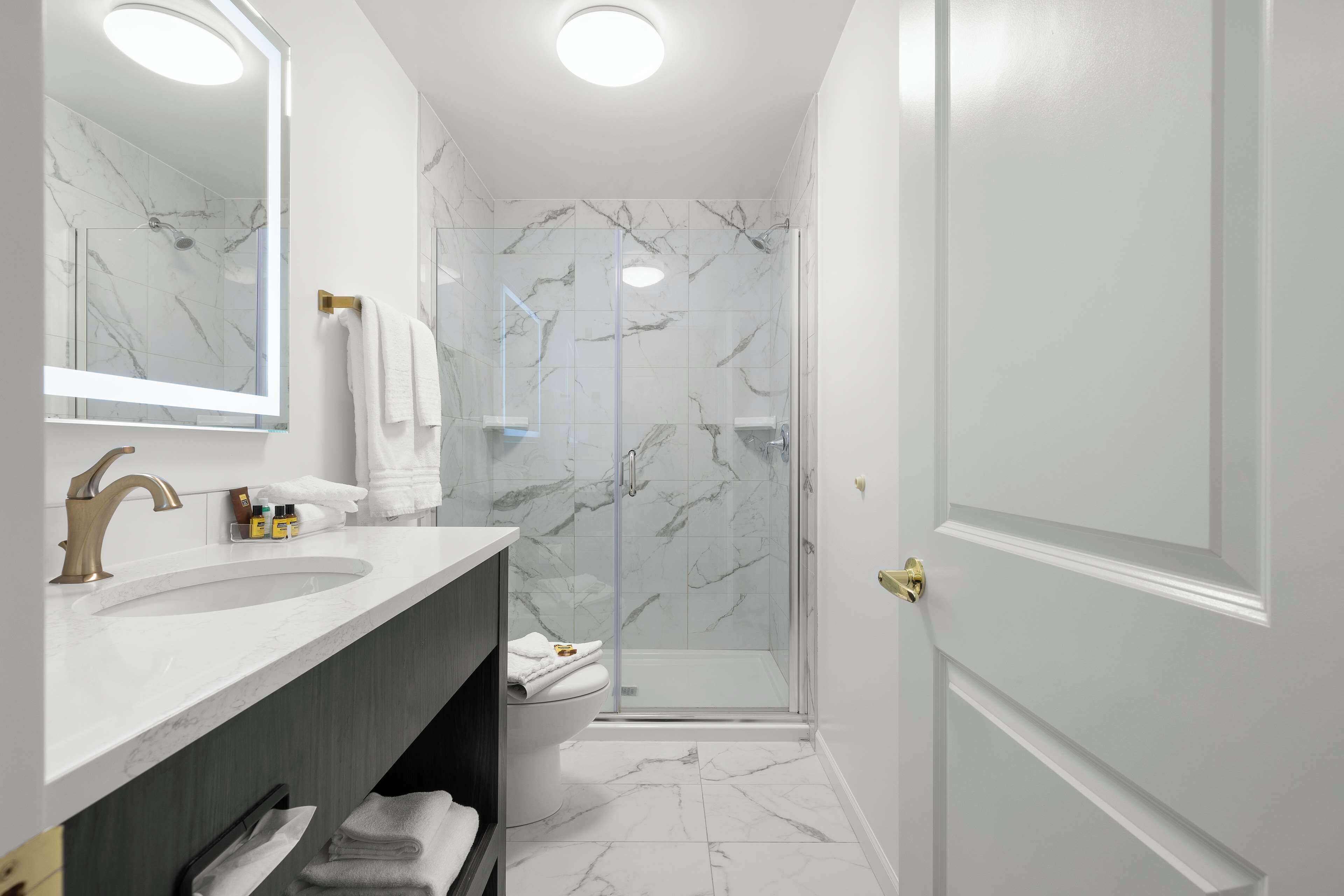 Un baño moderno con un lavabo de mármol, cabina de ducha con paredes de vidrio y una puerta blanca.
