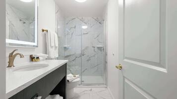 Un baño moderno con un lavabo de mármol, cabina de ducha con paredes de vidrio y una puerta blanca.