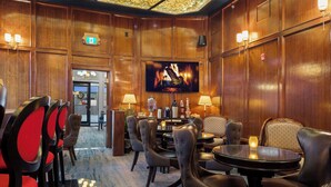 Un vestíbulo de hotel con paneles de madera, chimenea, televisor y zona de bar con sillones y mesas de cuero.