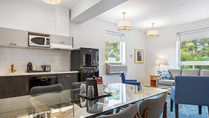 Una habitación de hotel moderna con una mesa de comedor de vidrio, un refrigerador negro, un microondas y una zona de estar con un sofá y sillones azules.