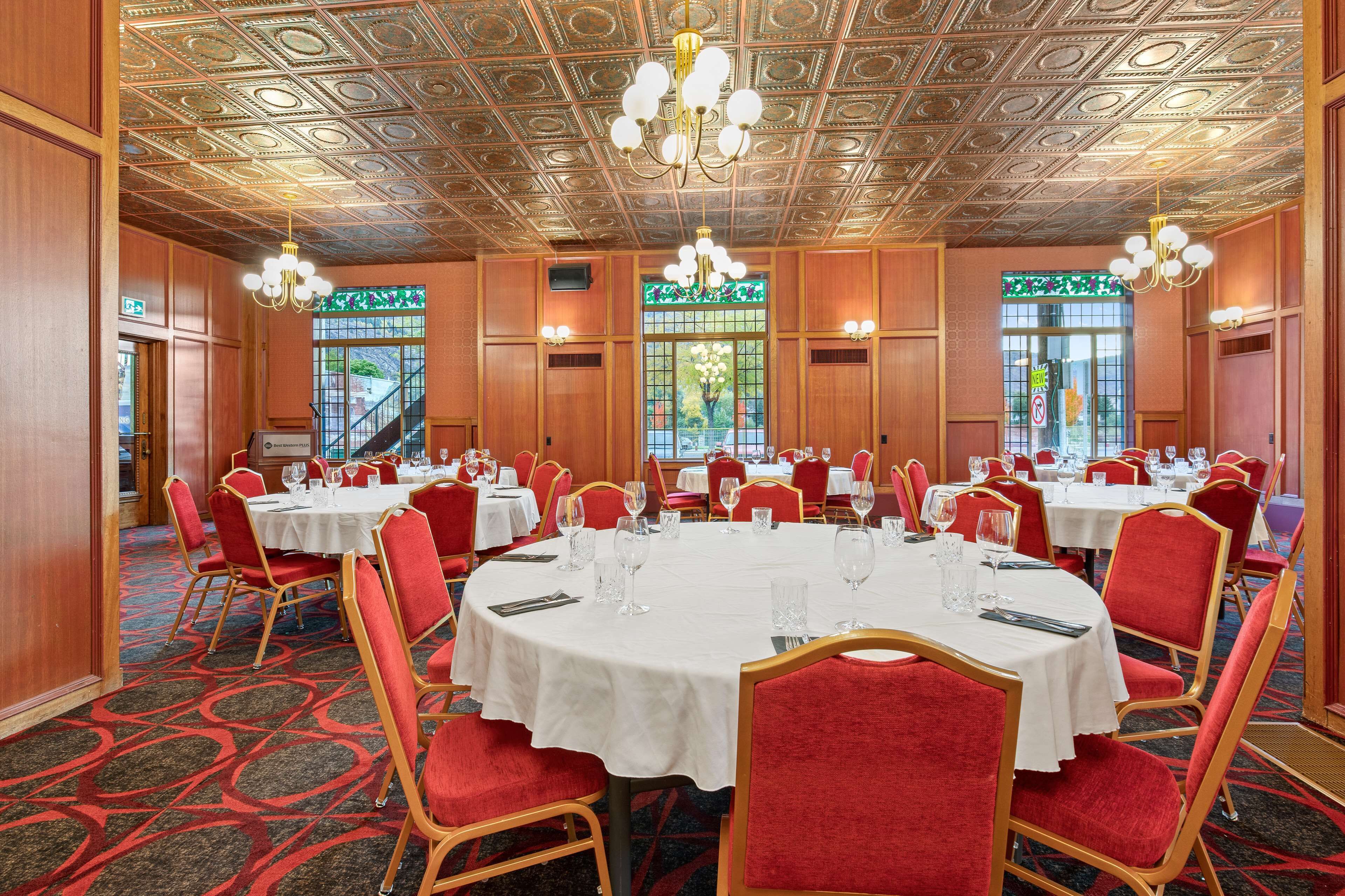 A banquet hall with round tables, red chairs, and a patterned ceiling.