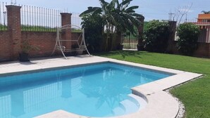Une piscine rectangulaire bordée de béton, entourée d’un mur de briques et d’une clôture en métal.