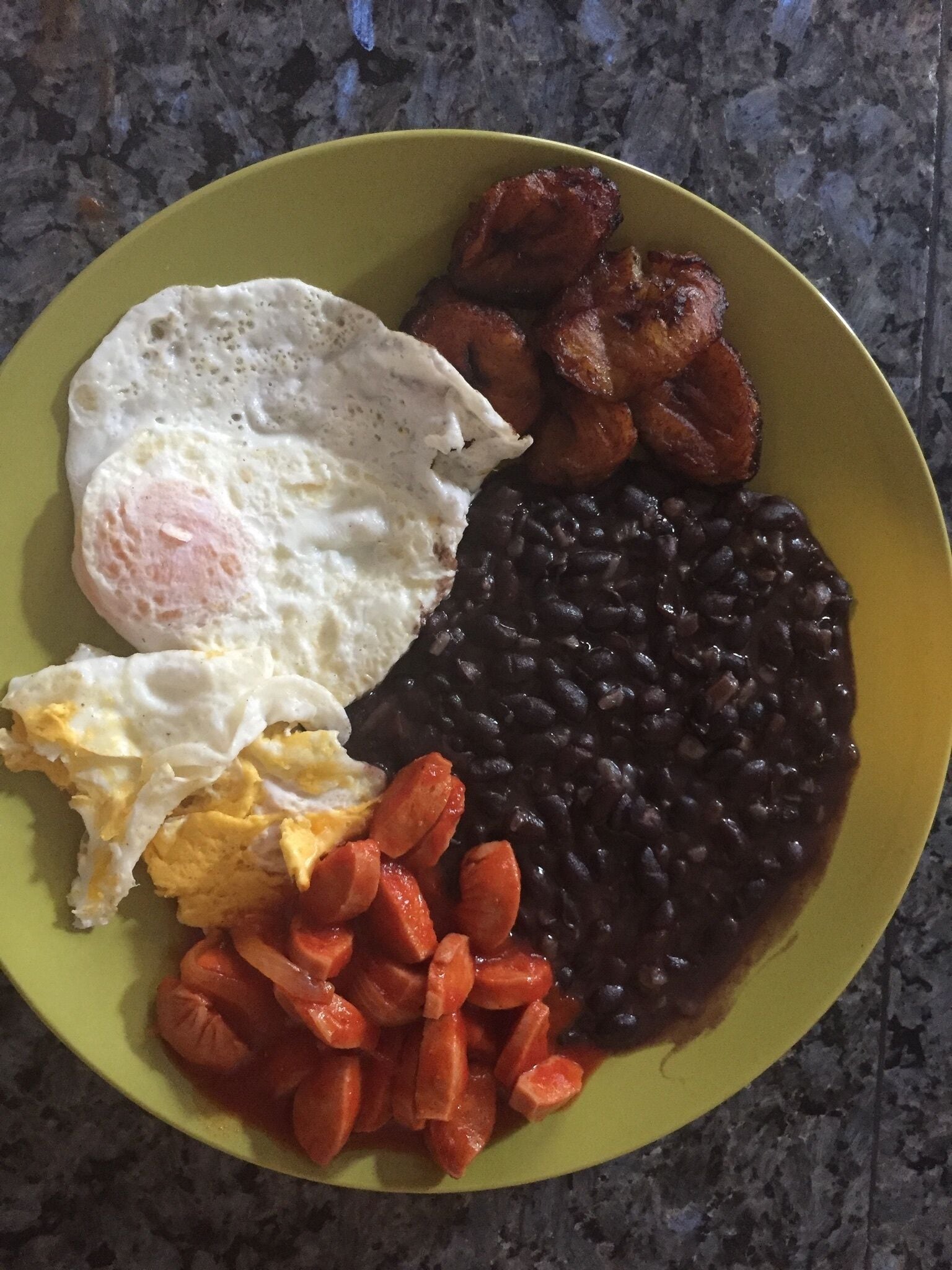 A plate with fried eggs, black beans, and sliced carrots.