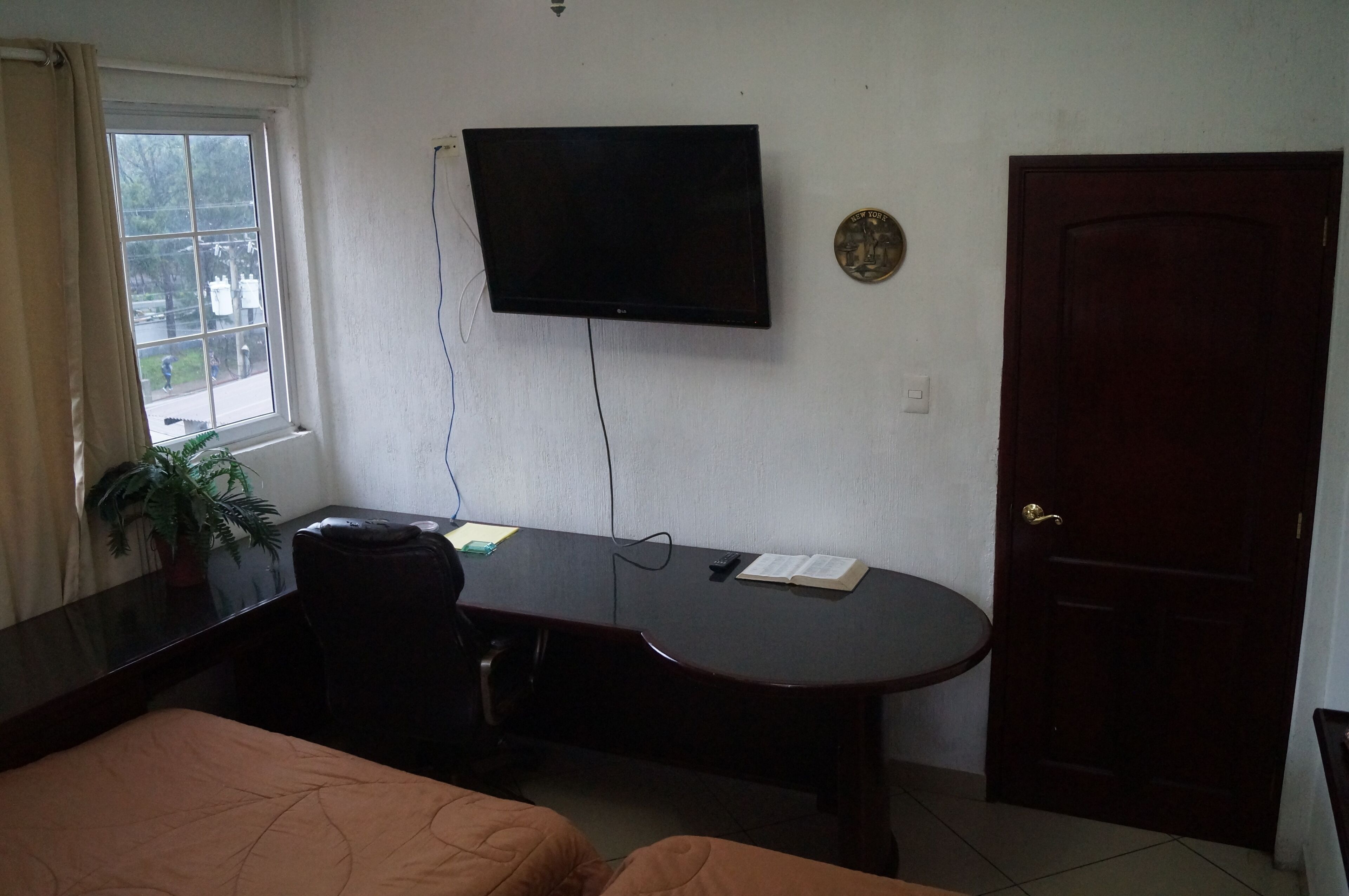 A hotel room with a bed, a desk, a television, a door, and a window.