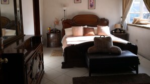 Ein Schlafzimmer mit einem hölzernen Bett, einem großen Spiegel, einer Kommode und einem Fenster mit Vorhängen.