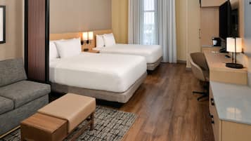 A hotel room with two beds, a sofa, a desk, and a television.