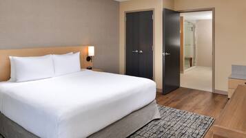 Quarto de hotel com cama grande, mesa de cabeceira, abajur, guarda-roupa e escrivaninha.