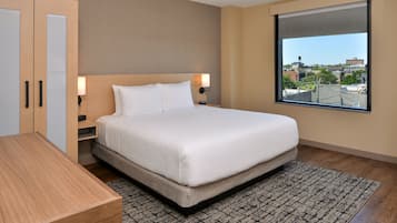 Une chambre d’hôtel moderne avec un grand lit, une armoire en bois, des tables de chevet et une vue sur la ville par une grande fenêtre.