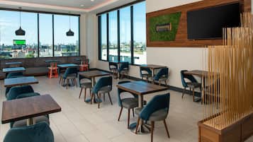 A modern restaurant with large windows, multiple seating areas, and a flat-screen TV mounted on the wall.
