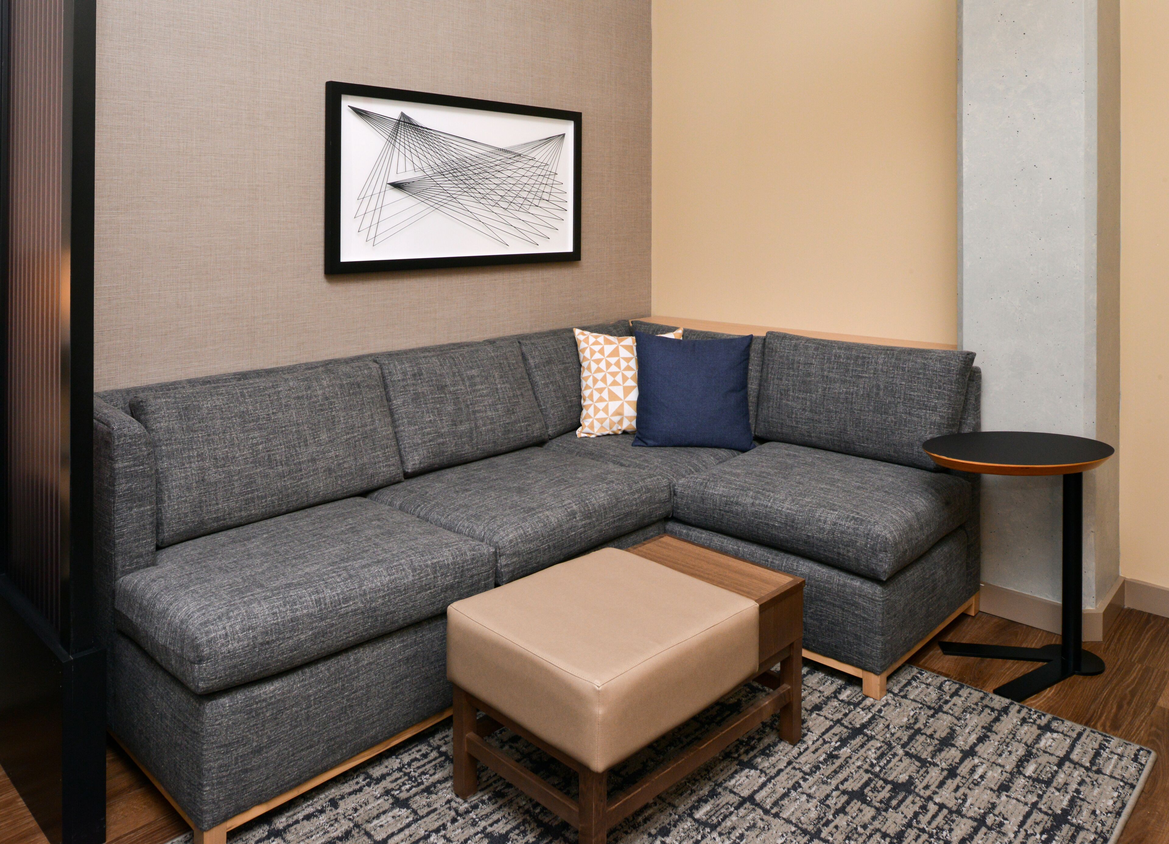 A gray sectional sofa with a wooden bench, a small round table, and a framed abstract artwork on the wall.