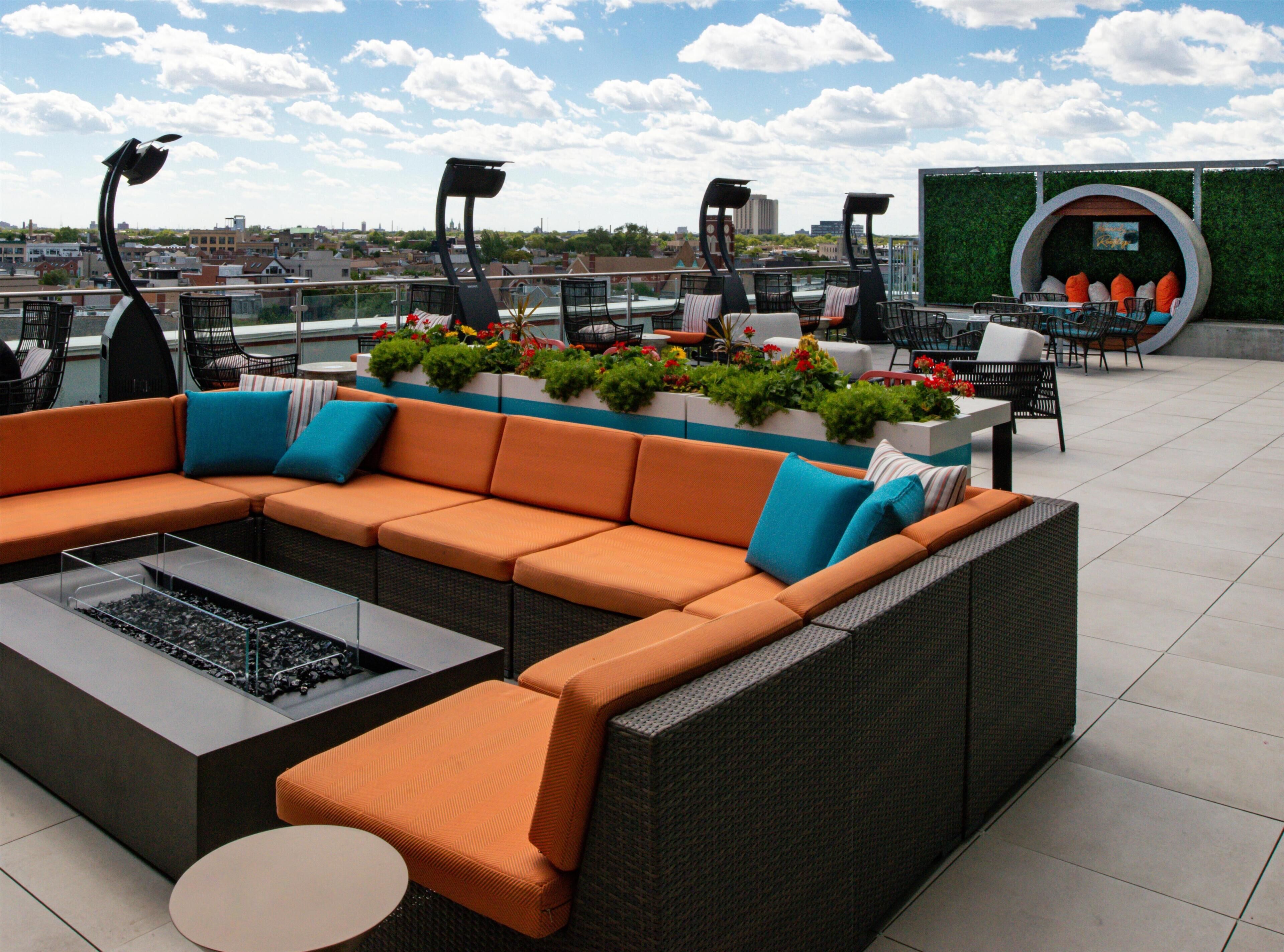 A rooftop terrace with a sectional sofa, outdoor furniture, and a decorative planter with flowers.