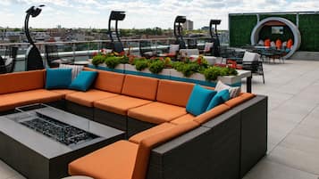 A rooftop terrace with a sectional sofa, outdoor furniture, and a decorative planter with flowers.