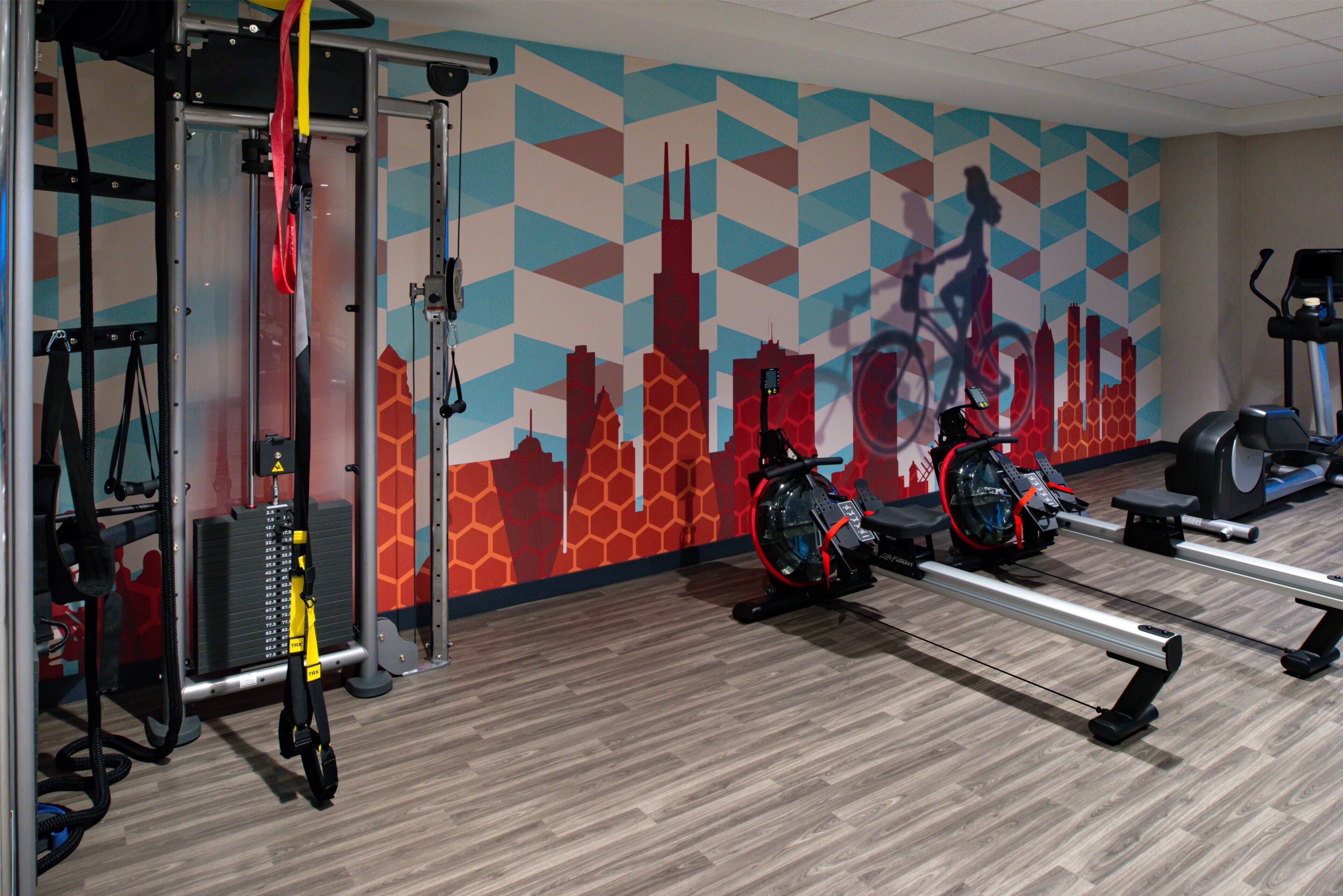 A gym with exercise equipment, a cityscape mural, and a wooden floor.